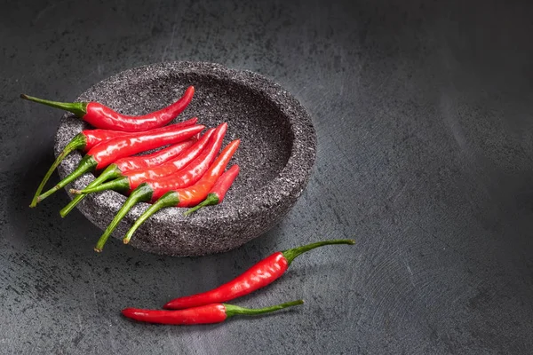 Close-up op rode hete chili paprika 's in stenen kom over donkere textuur — Stockfoto