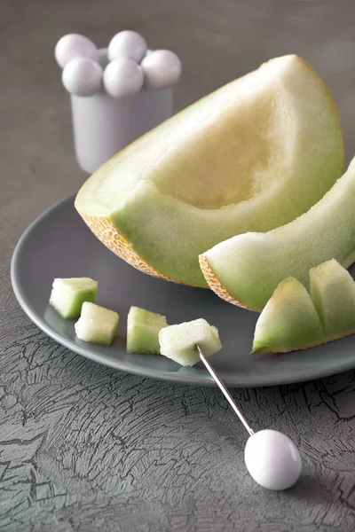 Cantaloupe melone on gray plat, with a piece is on a fruit stick — Stock Image Cantaloupe melone on gray plat, with a piece is on a fruit stick Stock Picture