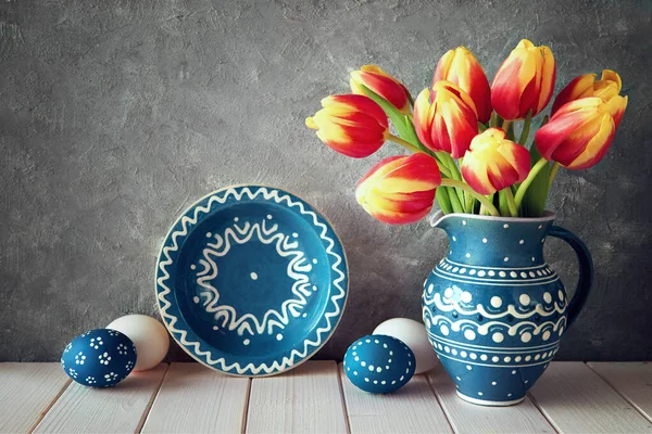 Tulipas vermelho-amarelas em jarro de cerâmica azul com ovos de Páscoa e um — Fotografia de Stock