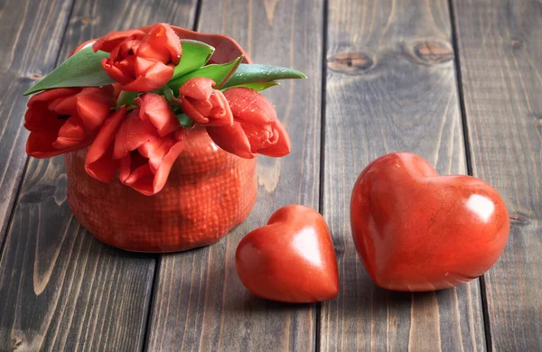 Two stone hearts and bunch of red tulips on wooden background — 스톡 사진