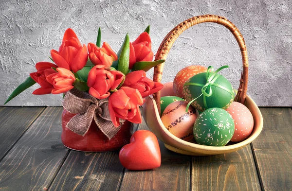 Composição de Páscoa com tulipas vermelhas, coração de madeira e uma cesta de — Fotografia de Stock