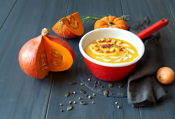 Pumpkin cream soup in red enamel pot on dark wood — Stock Photo, Image