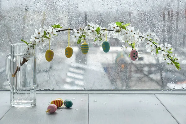 Ovos de Páscoa pendurados em galho com flores brancas pela janela — Fotografia de Stock