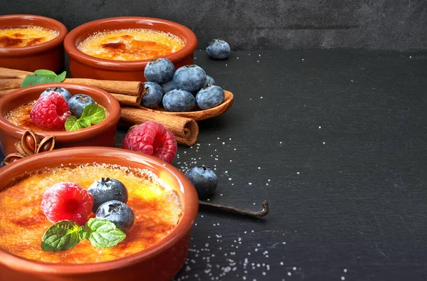 Creme brulee s bobulemi a ingrediencemi na tmavém kameni, prostor — Stock fotografie