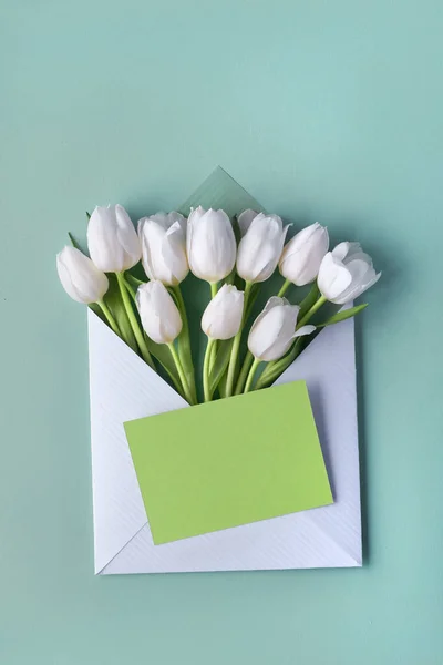 薄緑色のミントの背景に装飾的なハートステッカーと紙の封筒で白いチューリップ 春のフラットコピースペースとレイアウト — ストック写真