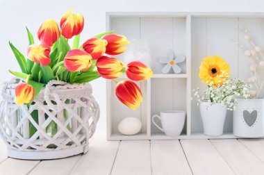 Kırmızı ve sarı laleli beyaz masa ve beyaz vitrinli bahar süslemeleri.