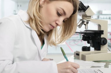 Genç kadın bilim adamı modern laboratuvarda yazıyor.