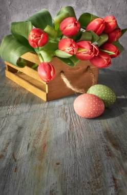 Bahar kutlaması arka planı: bir sürü kırmızı lale, bahar süslemeleri ve gri kırsal arka planda boyanmış yumurtalar, metin alanı