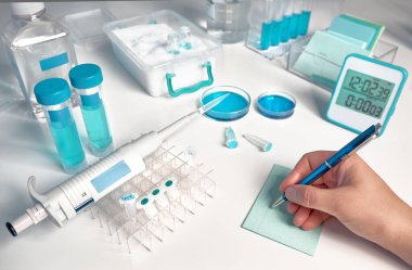 Bilimsel, tıbbi ya da eğitim geçmişi. Biyolojik ya da biyokimyasal laboratuvar odak dışı, kadın eline yakın plan bir not yazıyor.