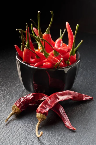 Close-up van verse rode chili paprika 's in zwarte keramische schaal en Dr. — Stockfoto
