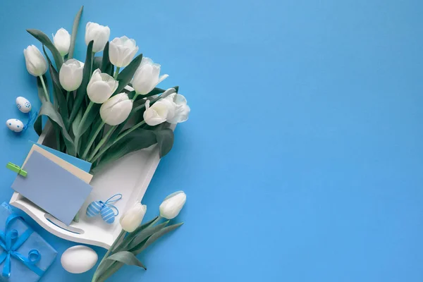 复活节边缘蓝皮书背景与复制空间 白色郁金香 包裹的礼物和白色盘子上的空白贺卡 调色的图像 — 图库照片