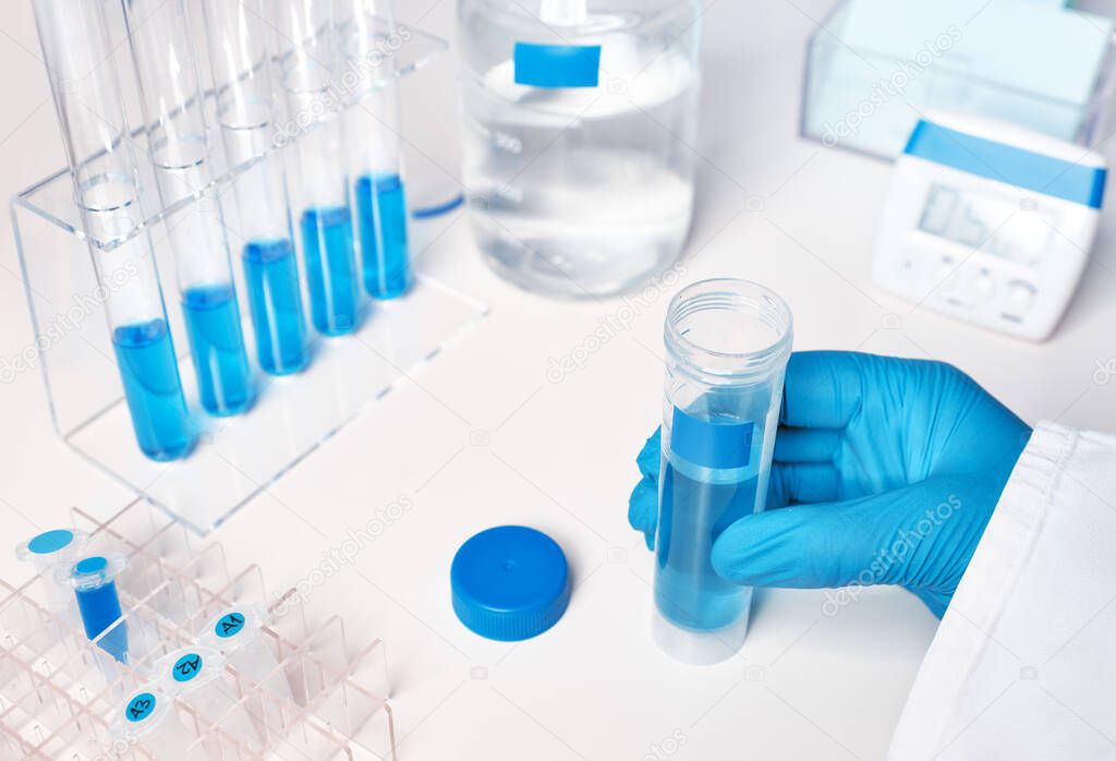 Liquid sample in gloved female hand, blue liquid samples in glas