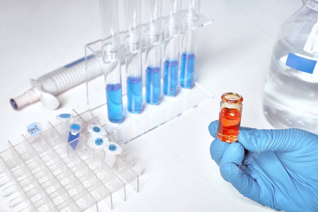 Liquid sample in female hand, blue liquid samples in glass tubes