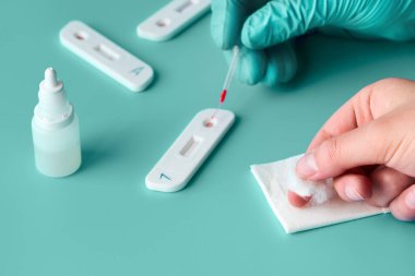 İgm ve IgG antikorları için COVID-19 testi yapın. Yeni Coronavirus SARS-CoV-2, Covid-19. Eldivenli hemşire kan testine pipetle giriyor. Hasta parmakları önde, yeşil nane arkaplanı..