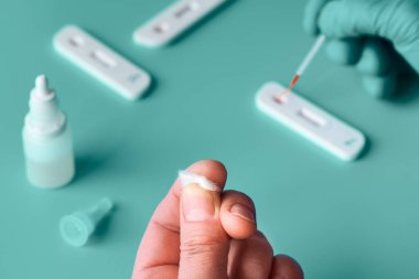 İgm ve IgG antikorları için COVID-19 testi yapın. Yeni Coronavirus SARS-CoV-2, Covid-19. Eldivenli hemşire kan testine pipetle giriyor. Hasta parmakları önde, yeşil nane arkaplanı..