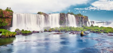 Arjantin 'de görkemli Iguazu şelaleleri. Sis ve bulutlarla dolu birçok görkemli ve güçlü su çağlayanlarının panoramik görüntüsü. Şelale ve taşların yansımasıyla Iguazu Vadisi 'nin panoramik görüntüsü.