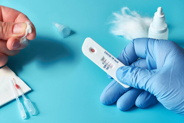 Express COVID-19 test for IgM and IgG antibodies to novel coronavirus SARS-CoV-2, Covid-19. Nurse hand in glove with positive test. Patient fingers with cotton. Vibrant turquoise background.