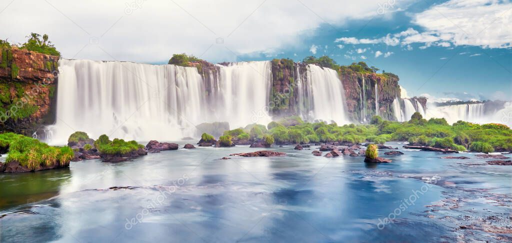 Majestic Iguazu waterfalls in Argentina. Panoramic view of many majestic powerful water cascades with mist and clouds. Panoramic image of Iguazu valley with reflection of waterfall and stones.