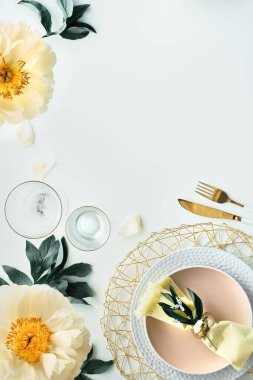 Beyaz masa üzerinde şakayık çiçekleri ve altın çatal bıçaklarla çağdaş masa. Modern modayla döşenmiş, sarı ve yeşille dekore edilmiş bir masa. Pentecost pfingstenrosen tasarımı, kopyalama alanı.