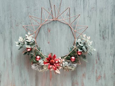 Kışın yeşil yaprakları ve kırsal ahşap kapıdaki geometrik altın metal çerçeveli çiçekleri olan geleneksel geleneksel Noel çelengi.