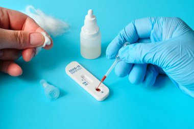 IgM için COVID-19 testi, yeni Coronavirus SARS-CoV-2 için IgG antikorları, Covid-19. Mavi eldivenli hemşire Corona virüsü testine kan uygular. Pamuklu parmaklar. Turkuaz arkaplan.