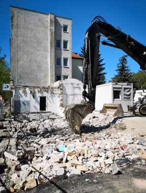 Şehir merkezindeki bir yıkım alanında kazıcı küreği. Arka planda bir konteynır ve kozalaklı ağaçlık ve ön planda çakıl taşı.