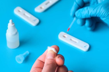 İgm ve IgG antikorları için COVID-19 testi yapın. Yeni Coronavirus SARS-CoV-2, Covid-19. Eldivendeki doktor, kan testine pipetle kan uygular. Hasta parmaklar, mavi nane arkaplanı.
