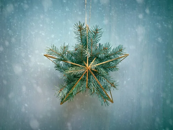 Christmas door decoration, golden metal star with Xmas fir twigs decorating light textured door. Digital snow effect.