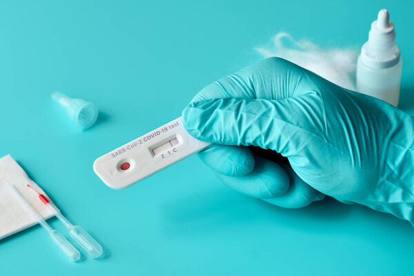 Express COVID-19 test for IgM and IgG antibodies to novel coronavirus SARS-CoV-2, Covid-19. Nurse or medtech hand in glove with positive coronavirus test. Vibrant turquoise background.