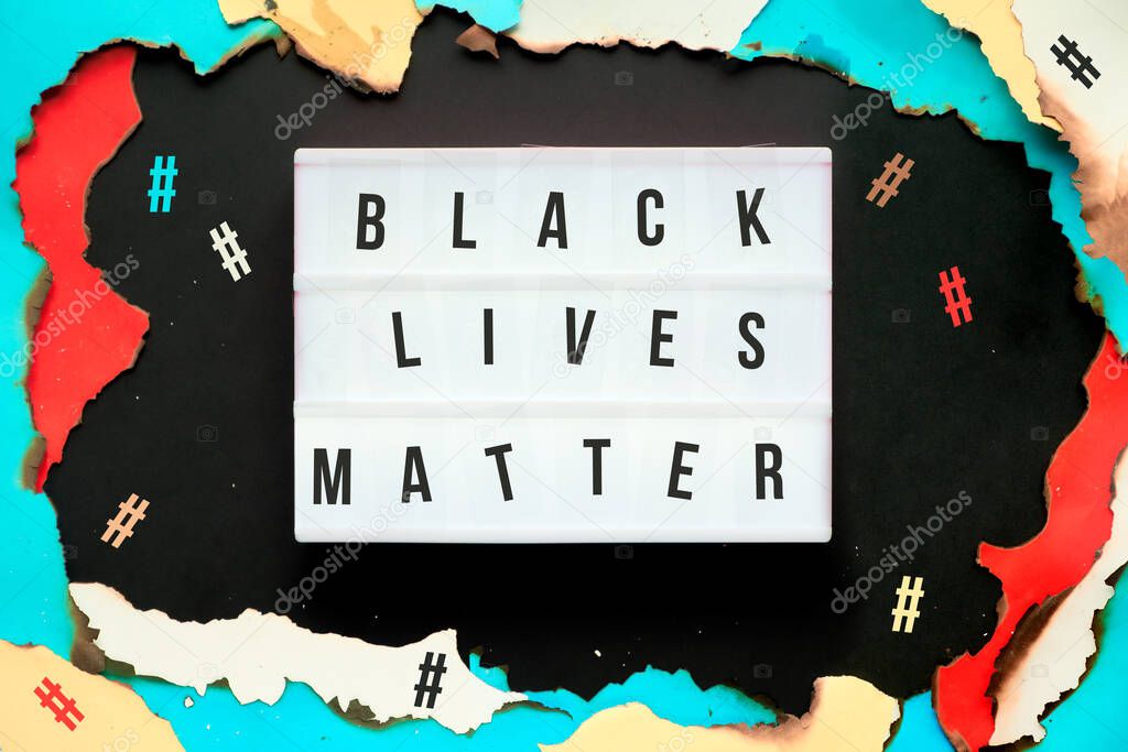 BLM movement. Paper hole with burned edges, text Black Lives Matter on lightbox, hashtags around. Protest, demonstration, movement against racism, racial discrimination.