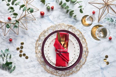 Kırmızı peçete, altın çatal bıçak ve beyaz mermer arka planda taze okaliptüs yapraklarıyla Noel sofrası. Düz yatıyordu, altın çatal bıçak takımları, beyaz tabaklar ve geometrik altıgenlerle birlikte masanın üstünde duruyordu..