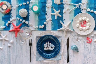 Mavi çizgili deniz süslemeleriyle Kolomb Günü öğle yemeği masası, klasik mavi beyaz tabaklar, kırsal masadaki çatallar. Manzaralı, gündelik modern öğle yemeği tabağında deco yelkenli gemi.