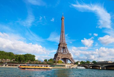 Güneşli bir günde Eyfel kulesiyle Paris şehri manzarası. Seine Nehri 'ndeki turist tekneleri. Mavi gökyüzünde tüy bulutlarıyla aydınlık güneşli bir gün..