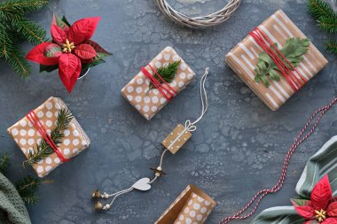 Noel hediyelerinin paketlenmesi, hediyeler, el işi kağıtları, soyut noktalar ve çizgiler olan kahverengi kağıtlar. Ahşap oyuncaklar, dekorasyonlar. Noel arkaplanı hediye kutuları, köknar dalları, koyu gri masa üzerindeki tekstil..