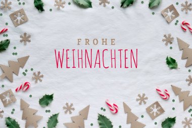 Frohe Weihnachten 'a Almanca Mutlu Noeller demek. El işi kağıdından çevre dostu dekorlar, kırmızı beyaz baston şekerler ve doğal yeşil kutsal yapraklar. Xmas ağaç siluetleri, kar taneleri ve daireler.