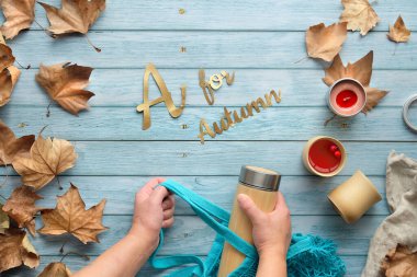 Kadın elleri, çevre dostu ağ torbası ve bambu termos şişesini tutuyor. Sonbaharda sıfır ziyan çayı, Sonbahar için A mesajı. Bambu bardakları ve dağınık sonbahar yapraklarıyla solmuş ahşap masada yatıyordu..