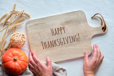 Eller kesme tahtasıyla delik deşik oldu. Mutlu Şükran Günleri. Sonbahar süslemeleri, altın buğday kulakları ve turuncu balkabağı. Üst görünüm, düz masa üzerinde beyaz tekstil masa örtüsü ile.