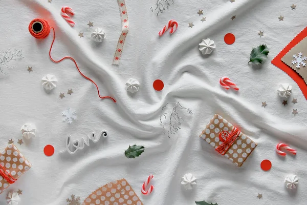 Kış tatili için el yapımı dekorasyonlar. El işi ambalaj kağıdında hediye kutuları, kutsal, kahverengi ve kırmızı kağıt siluetler, şekerlemeler. Çevre dostu kış kutlaması. Düz beyaz tekstil yatıyordu.