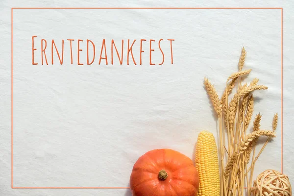 Erntedankfest means Thanksgiving in German language. Flat lay with natural harvest Autumn decorations, pumpkin, corn cob and wheat ears on white textile background.