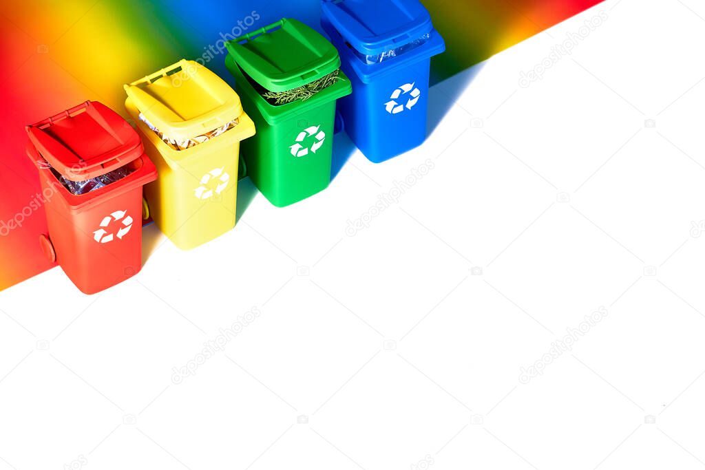 Four color coded recycle bins, isometric projection on geometric rainbow paper background with copy-space. Recycling sign on the bins - red, blue, yellow and green. Waste separation concept.