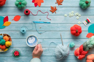 Bir fincan kahve, mavi latte. Yün yumakları, yün demetleri, dekoratif keçeli balkabakları ve sonbahar yapraklarıyla ahşap masa manzarası. Mevsimsel Sonbahar Solmuş hafif tahtaların üzerinde yatıyordu.