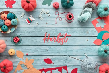 Yün demetlerden, iplik toplarından, süslü keçeli balkabaklarından ve renkli sonbahar yapraklarından yapılmış dekoratif çerçeve. Kağıt metin Herbst Almancada sonbahar anlamına gelir. Mevsimsel Sonbahar Açık mavi ahşap üzerine uzanır.