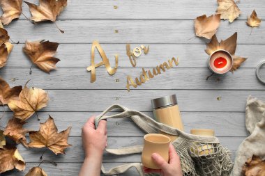 Kadın elleri ağ torbasını ve bambu termosunu tutuyor. Sonbaharda sıfır ziyan çayı, Sonbahar için A mesajı. Bambu bardakları ve dağınık sonbahar yapraklarıyla solmuş ahşap masada yatıyordu..