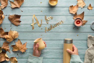 Sonbaharda sıfır atık kahve. Autumn 'un A metni. Elleri çevre dostu yalıtılmış metal matara ve bambu kabını tutuyor. Düz yatıyordu, üst görünüm yeşil nane ahşap zemin, el yapımı mum ve kuru yapraklarla..