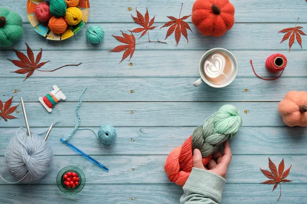 手を保持ウールバンドルとコーヒーカップ 糸玉で木製のテーブルの上からの眺め 装飾的な感じのカボチャと天然のカエデの葉 薄緑色の板に季節の秋のフラットレイ — ストック写真