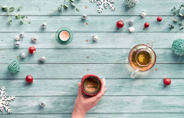 冬のお茶 ガラスティーポットとの配置 ライトブルーミントの木の背景に手にお茶のガラス クリスマスの装飾 ミラーボール ボール おもちゃ ティーキャンドル ユーカリ — ストック写真