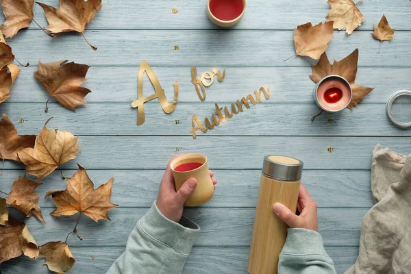 断熱魔法瓶フラスコと竹カップを保持手 秋に廃棄物ゼロ茶 秋の葉が散在する木製のテーブルの上にフラットレイアウト 秋のテキストA — ストック写真