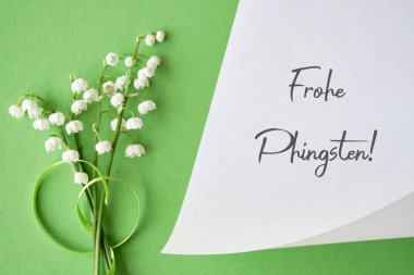 Lily of the valley flowers arranged on a green background with a white card featuring the text 