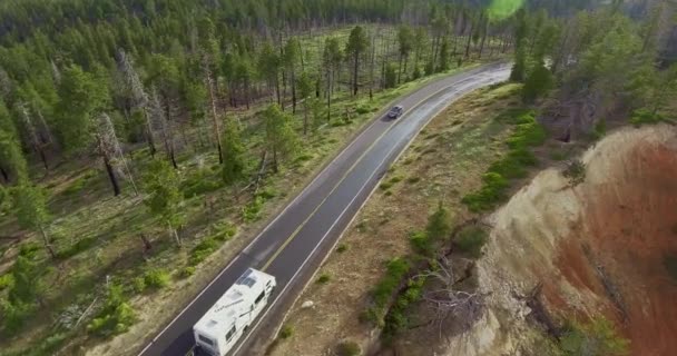 ドローンカメラは高さから離陸します車輪の上の旅の白い家と峡谷の崖の上の松林の高速道路上の今後の黒い車 シオン国立公園 ユタ州 アメリカ — ストック動画