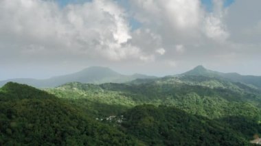 Drone kamera, üzerinde yerleşim ve ufukta sisli bulutlar (Aziz Lucia) ile ormanlık dağlar çeker.)